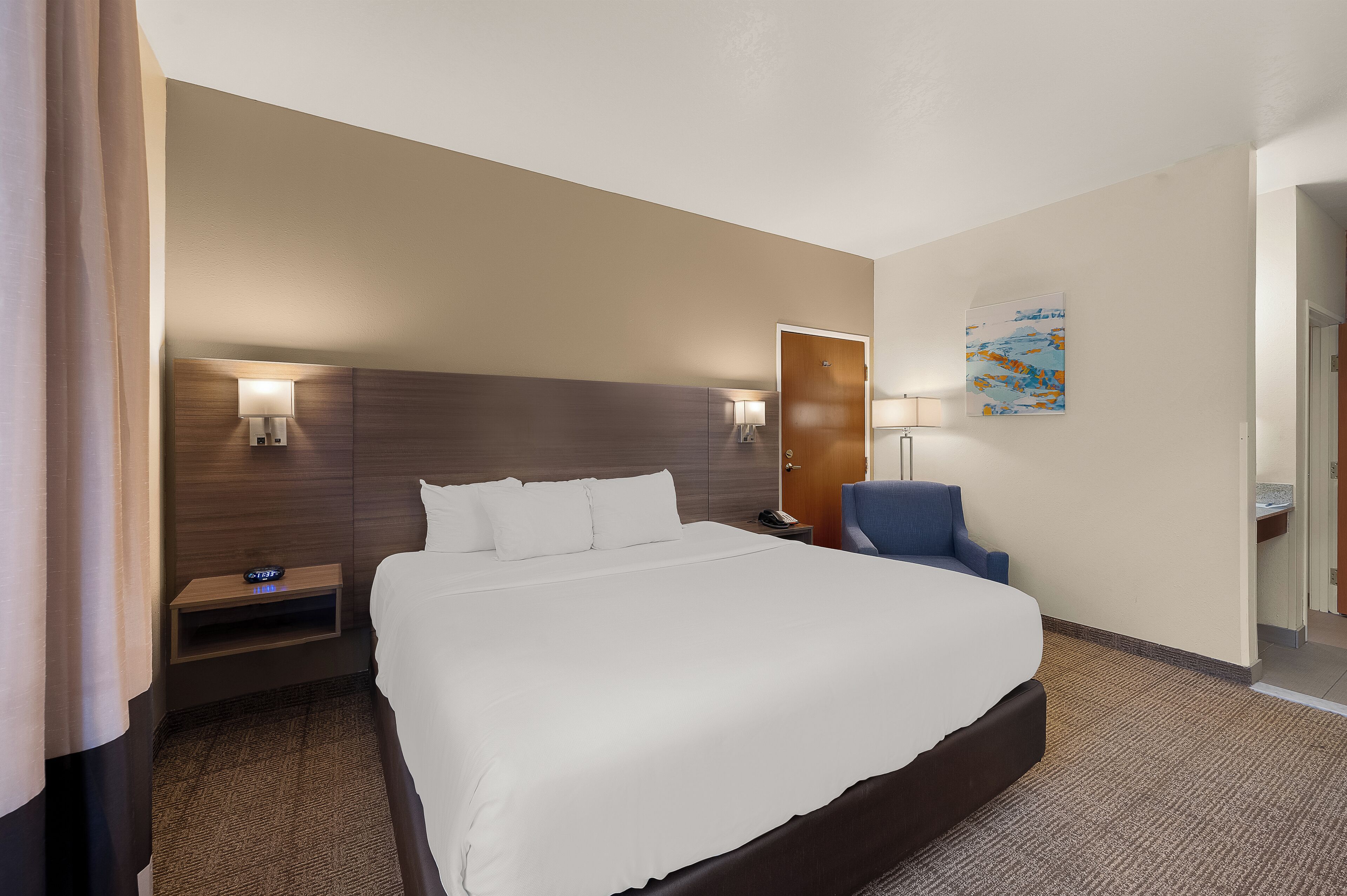A hotel room with a large bed, bedside tables, a chair, and a painting on the wall.