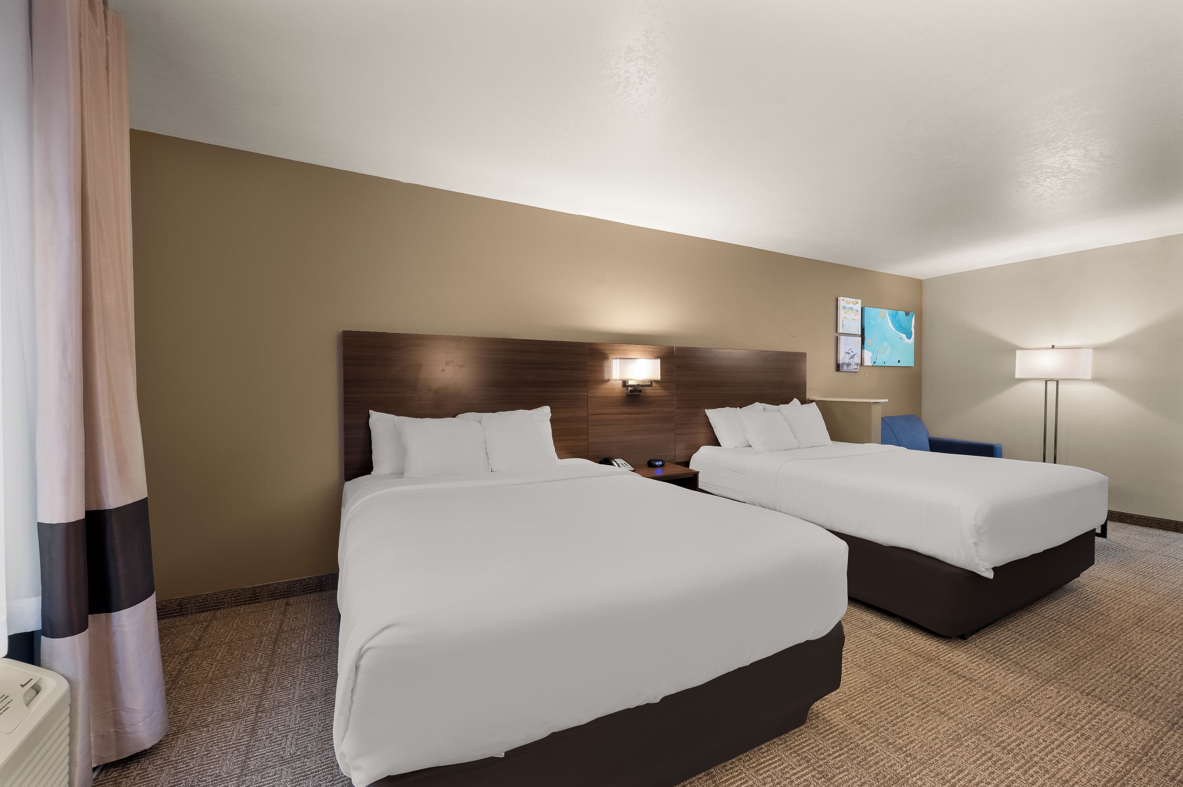 A hotel room with two beds, a nightstand, a lamp, and a wall-mounted artwork.