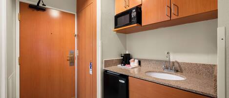 Una cocina compacta con armarios de madera, microondas, fregadero y lavavajillas.