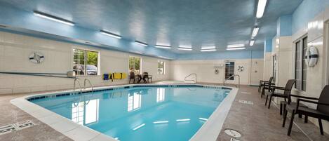 An indoor swimming pool with clear lane markings, safety signs, and a lifeguard chair.