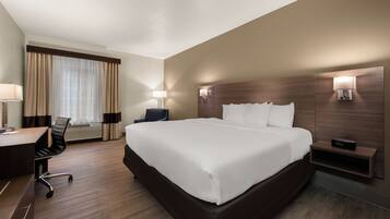 A hotel room with a large bed, a desk, a chair, a lamp, and a nightstand.
