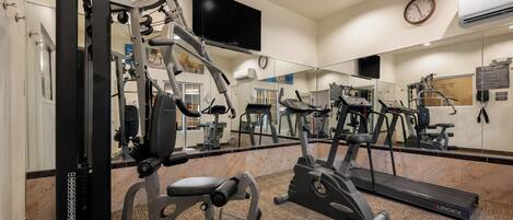 A gym with various exercise equipment, a large mirror, and a clock on the wall.