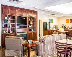 Habitación de hotel con kitchenette, un televisor de pantalla plana, un sofá, una mesa de comedor y un sillón pequeño.