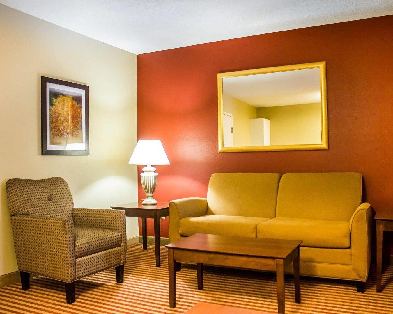 Una habitación con un sillón estampado, un sofá, una mesita, una lámpara y un cuadro en la pared.