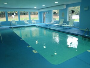 Ein Hallenbad mit klarem Wasser, Tiefenlinien und weißen Liegestühlen am Beckenrand.