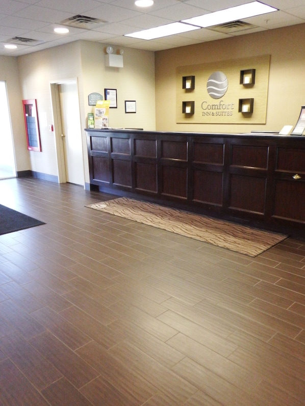 A reception area with a dark wood reception desk, a rug, and a wall sign that reads "Comfort Inn & Suites".