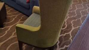 A living room with a green armchair, a blue sofa, and a dining area with wooden tables and chairs. - Comfort Inn & Suites Dayville - Killingly Industrial Park (Dayville)
