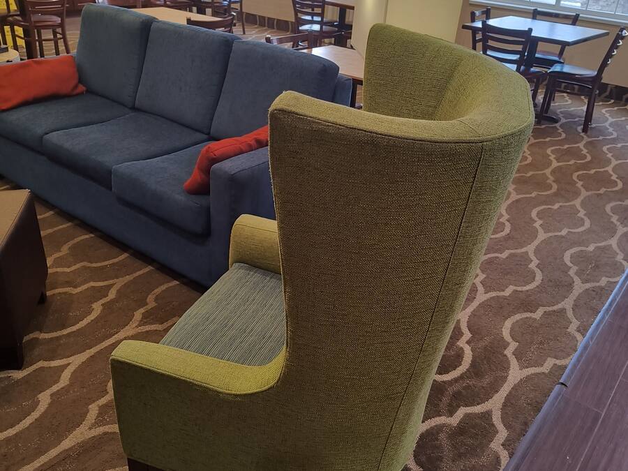 A living room with a green armchair, a blue sofa, and a dining area with wooden tables and chairs.