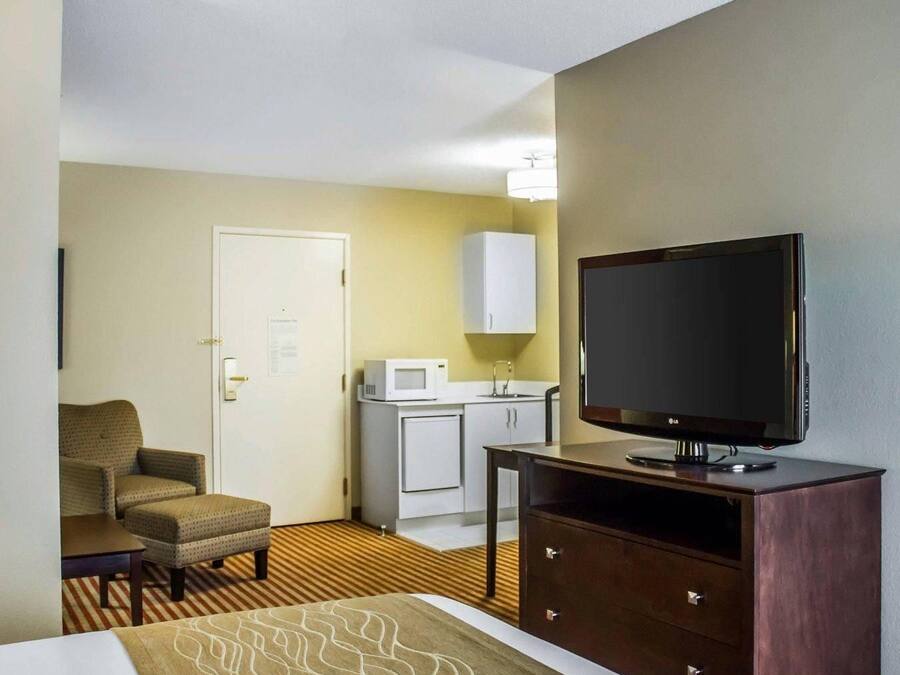 A hotel room with a bed, a television on a wooden stand, a microwave, a small cabinet, and a chair.