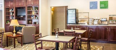 Comedor de hotel con mesas, sillas, televisor y una barra de buffet.