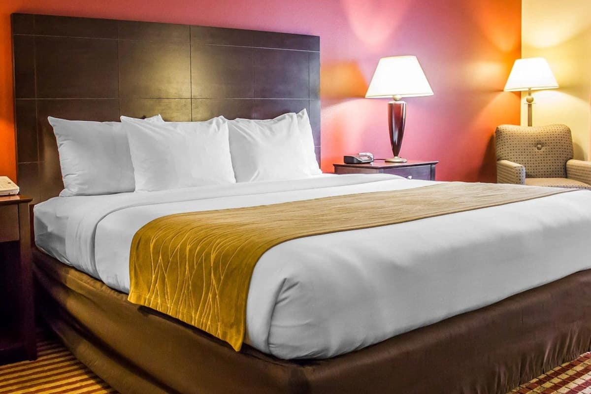 A hotel room with a large bed, two bedside tables, a chair, and a lamp.