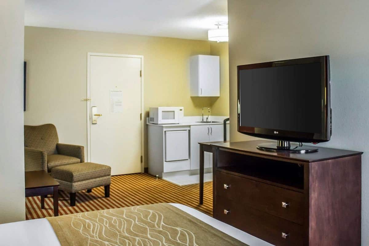 A hotel room with a bed, a TV on a wooden stand, a microwave, a small cabinet, and a chair.