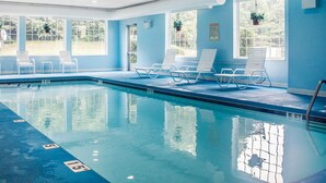 An indoor swimming pool with clear water, marked lanes, and white lounge chairs.