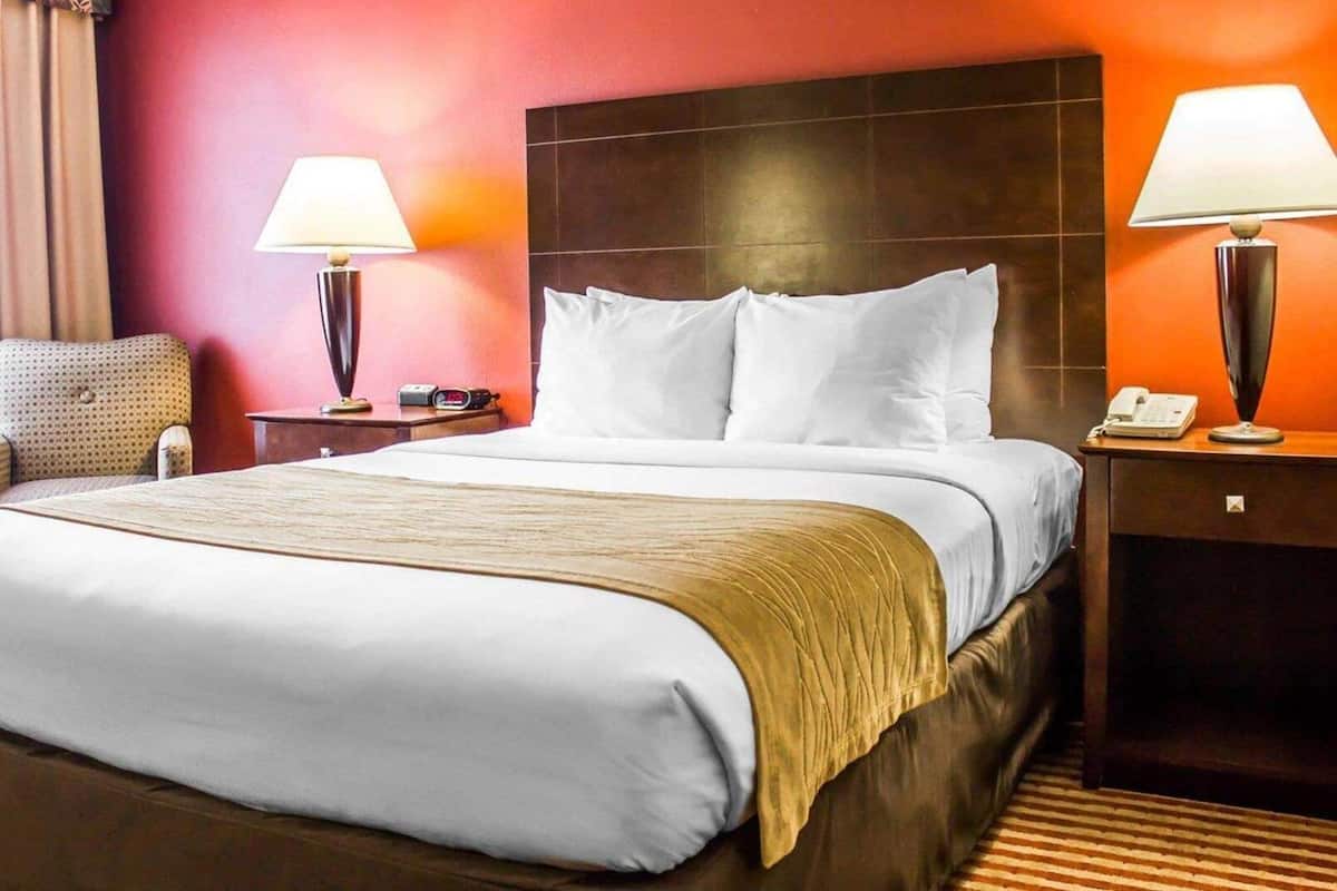 Een hotelkamer met een groot bed, twee nachtkastjes, een stoel en een rode wand.