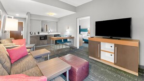 A modern hotel room with a sofa, ottoman, TV, kitchenette, and a dining area. - Hampton Inn & Suites Newtown (Morrisville)