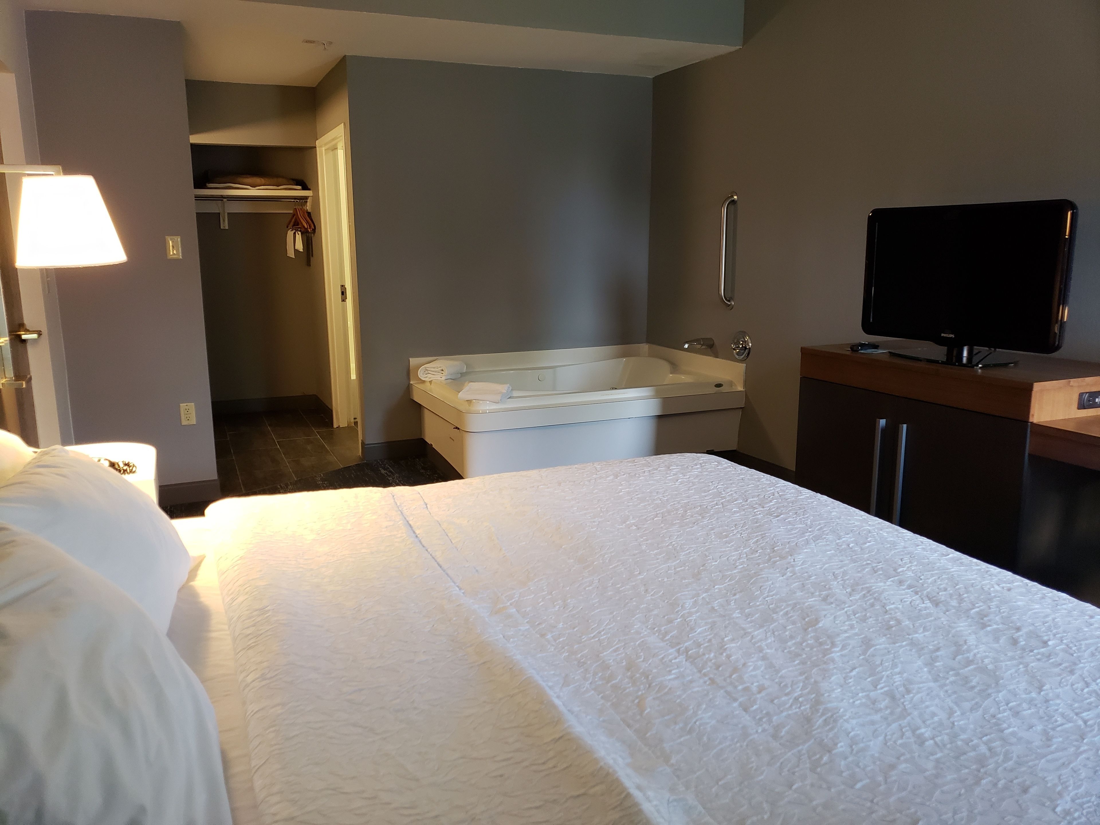 A hotel room with a bed, a TV, a bathtub, and a walk-in closet.
