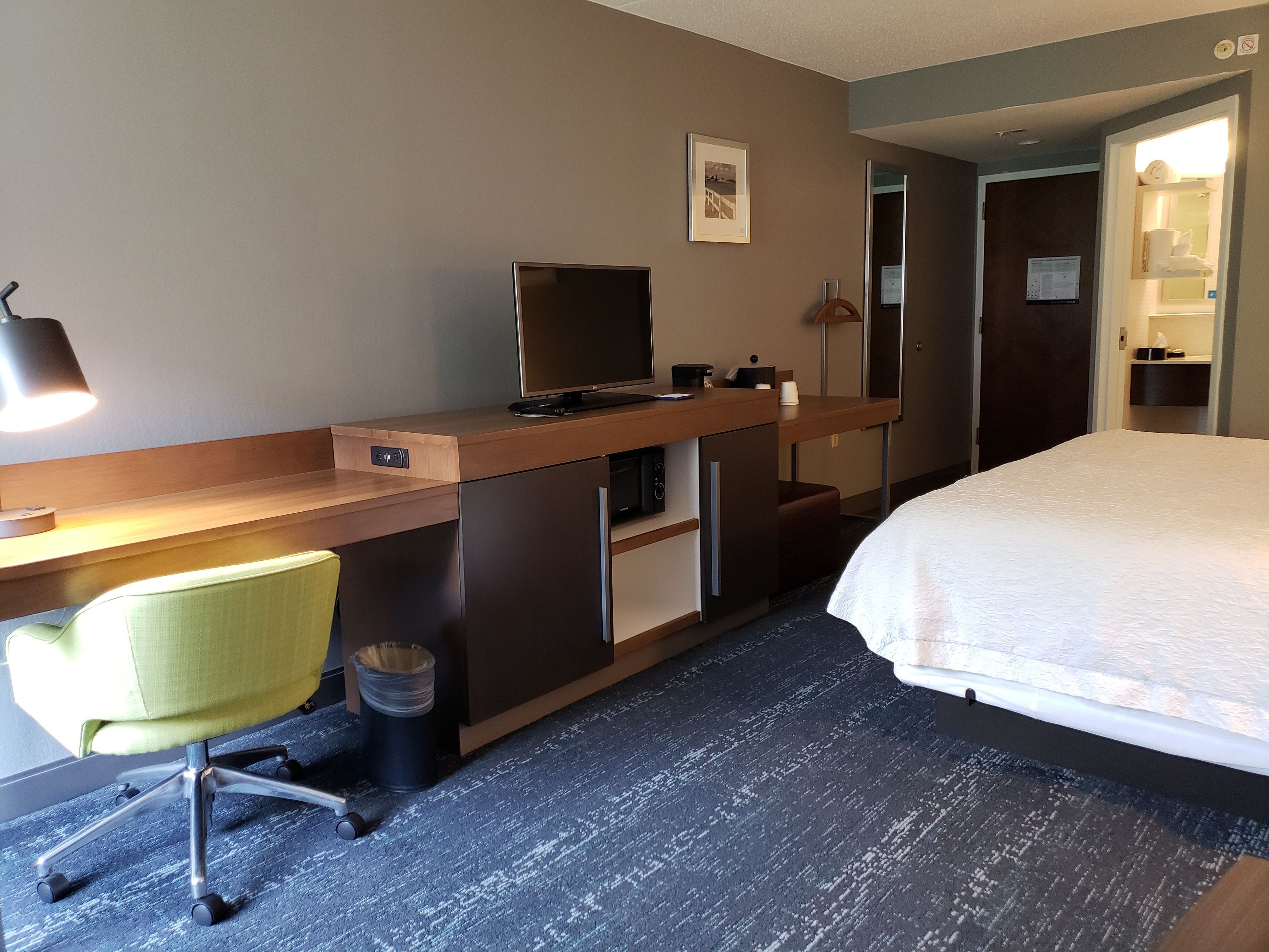 A hotel room with a bed, desk, chair, and a small kitchenette.