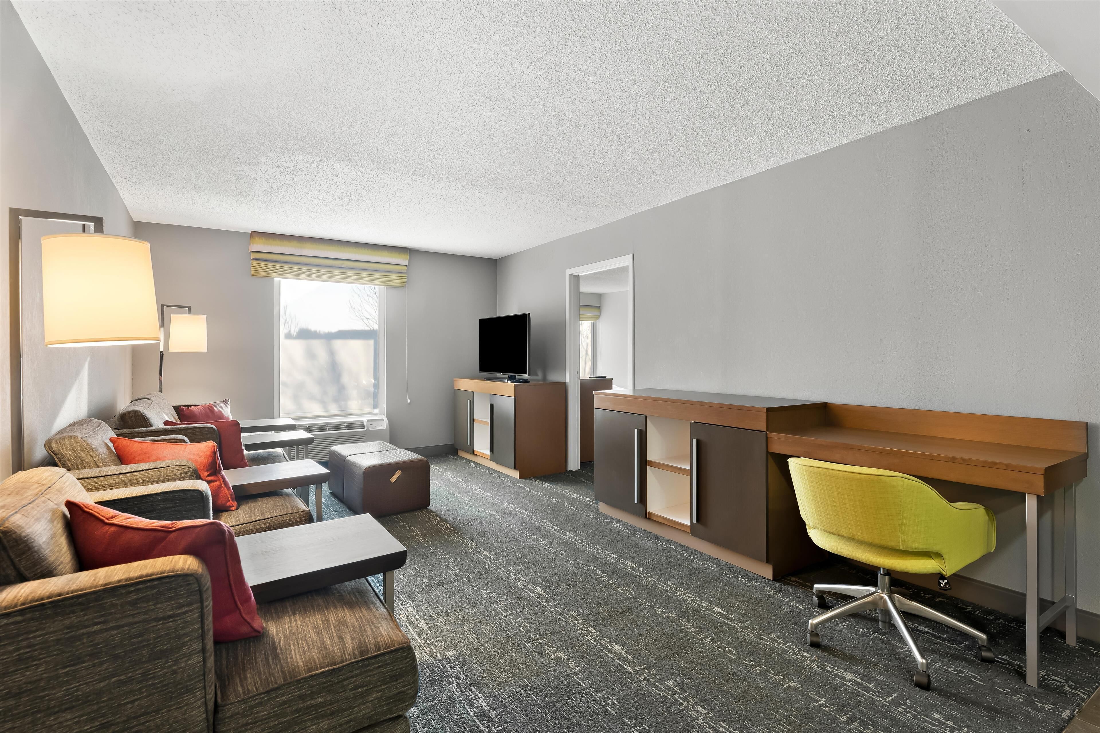 Habitación de hotel con un sofá, un escritorio con silla, televisor y ventana.