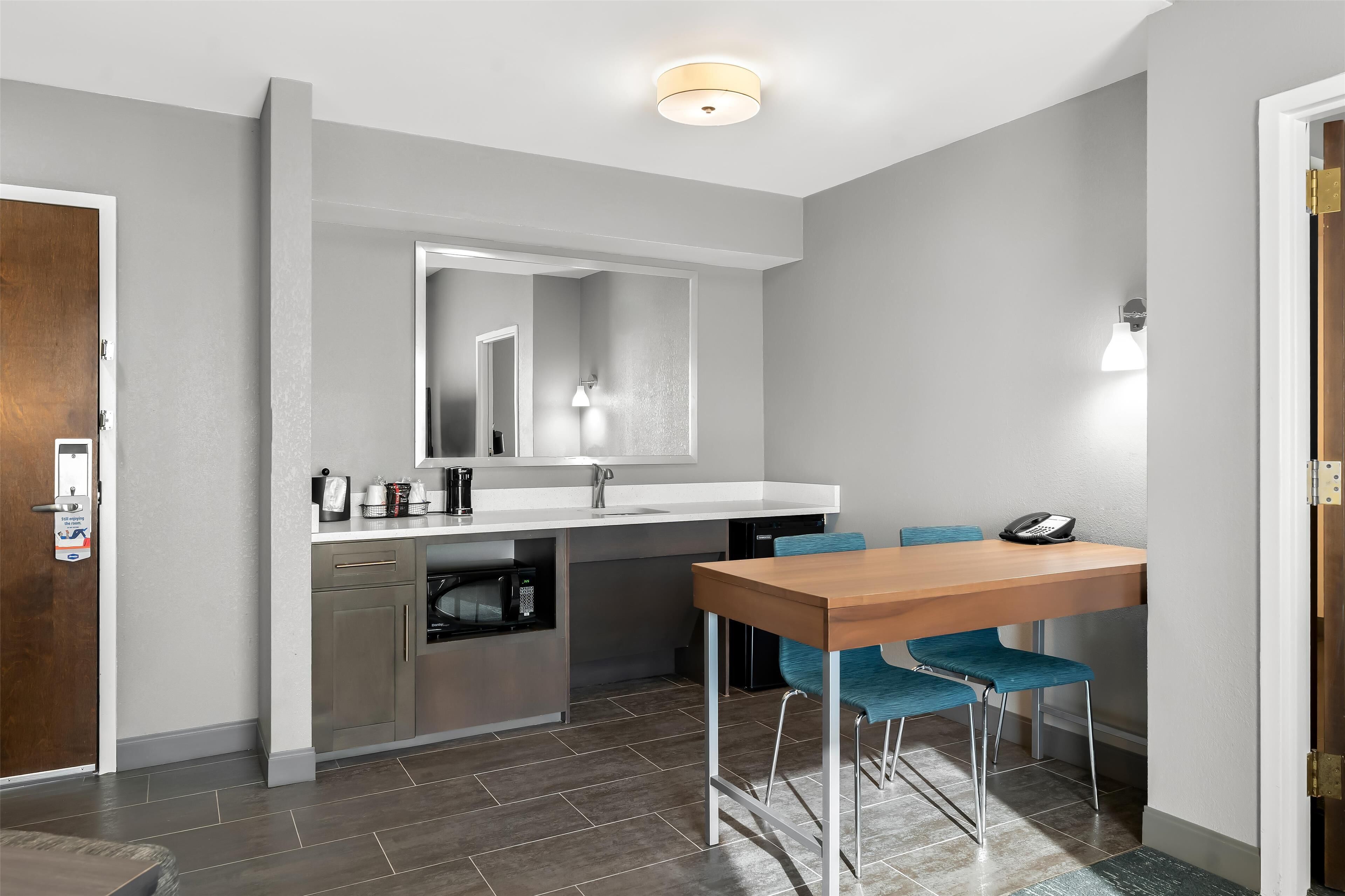 A compact kitchen with a wooden dining table and blue chairs, a built-in oven, and a microwave.