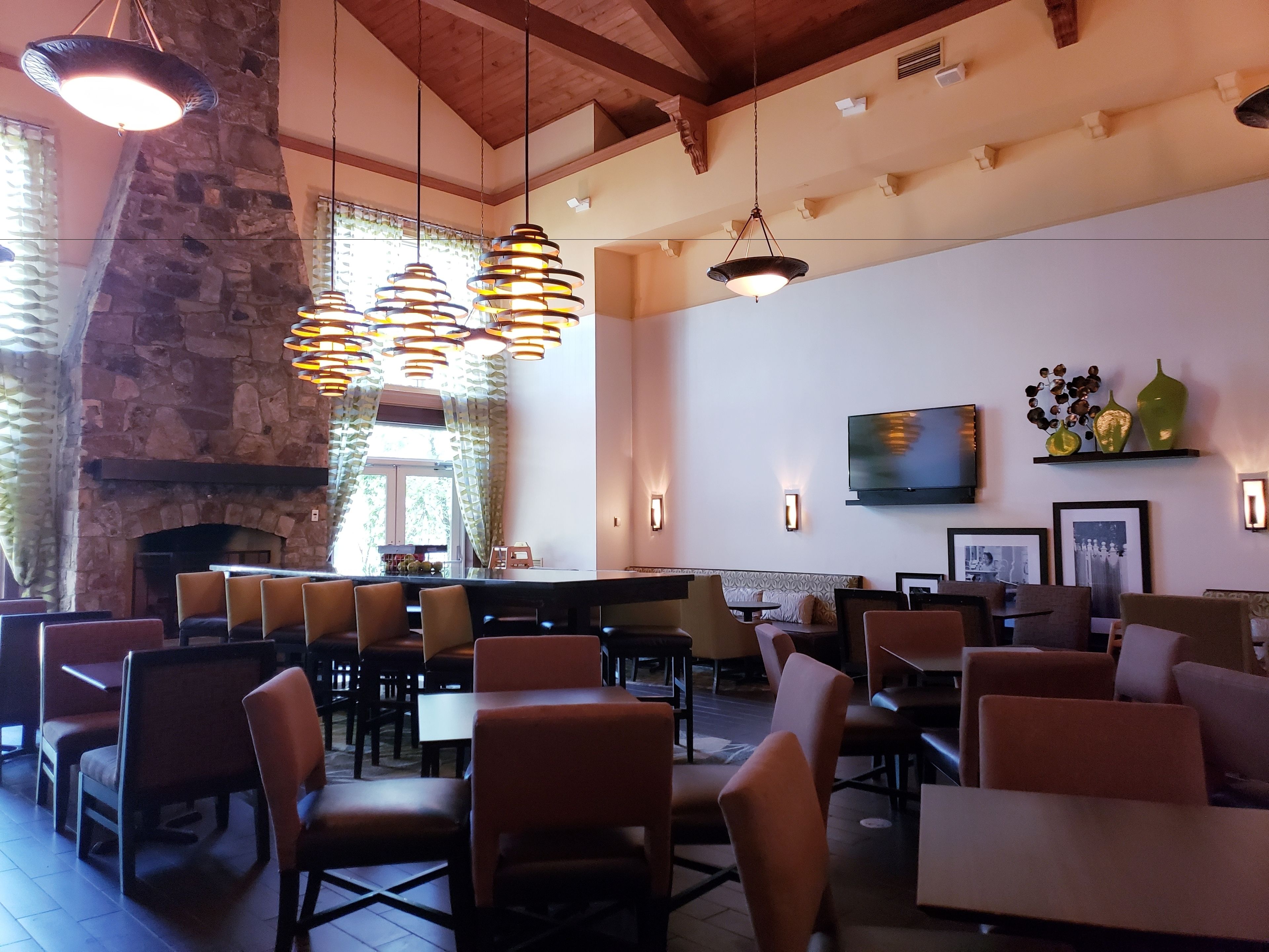 Un restaurante con paredes de piedra, lámparas colgantes y una chimenea. Las mesas y sillas están dispuestas para comer.