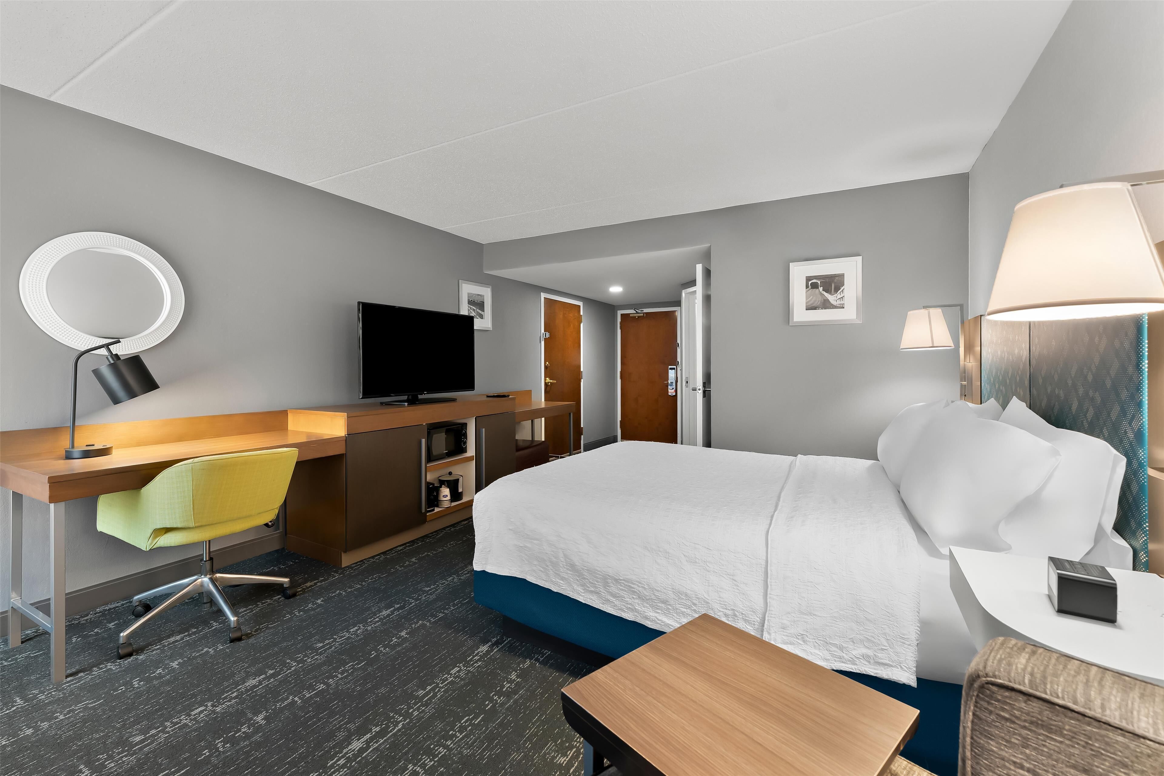 A hotel room with a bed, desk, chair, TV, and lamps.