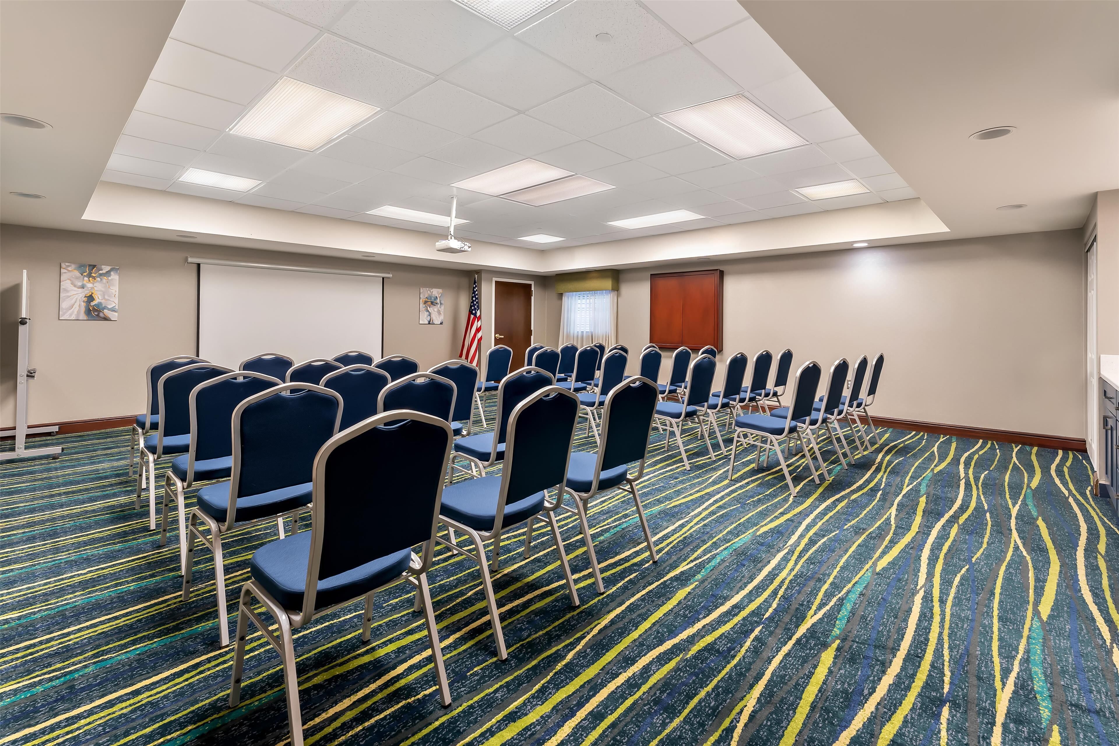 Une salle de conférence avec des rangées de chaises, un écran de projection et un drapeau américain.
