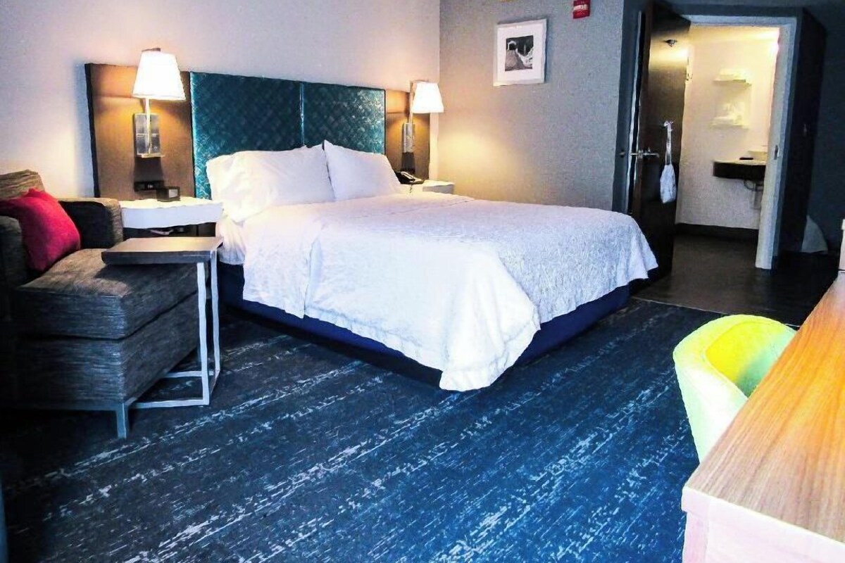 A hotel room with a bed, a desk, a chair, and a bathroom visible through an open door.