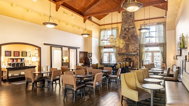 A spacious dining area with high ceilings, stone accents, and modern lighting fixtures. - Hampton Inn & Suites Newtown (Morrisville)