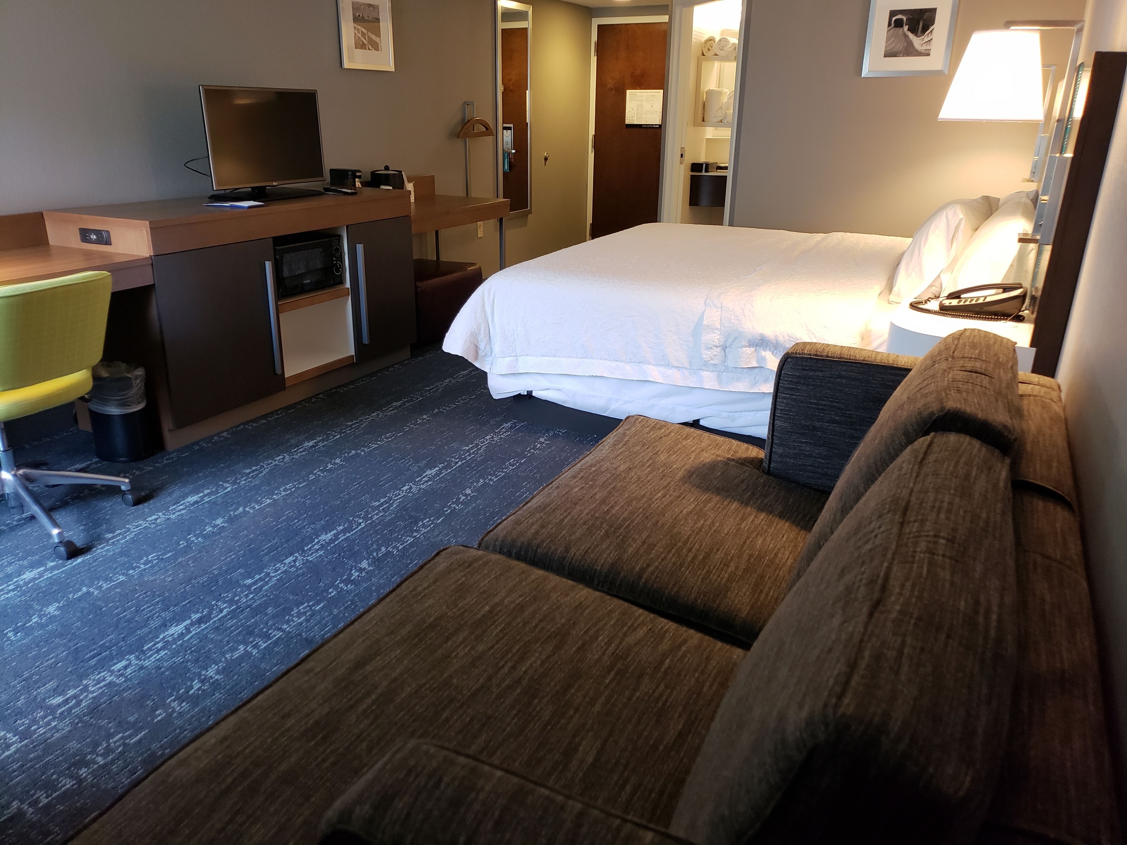 A hotel room with a bed, a desk with a computer, a chair, and a sofa.