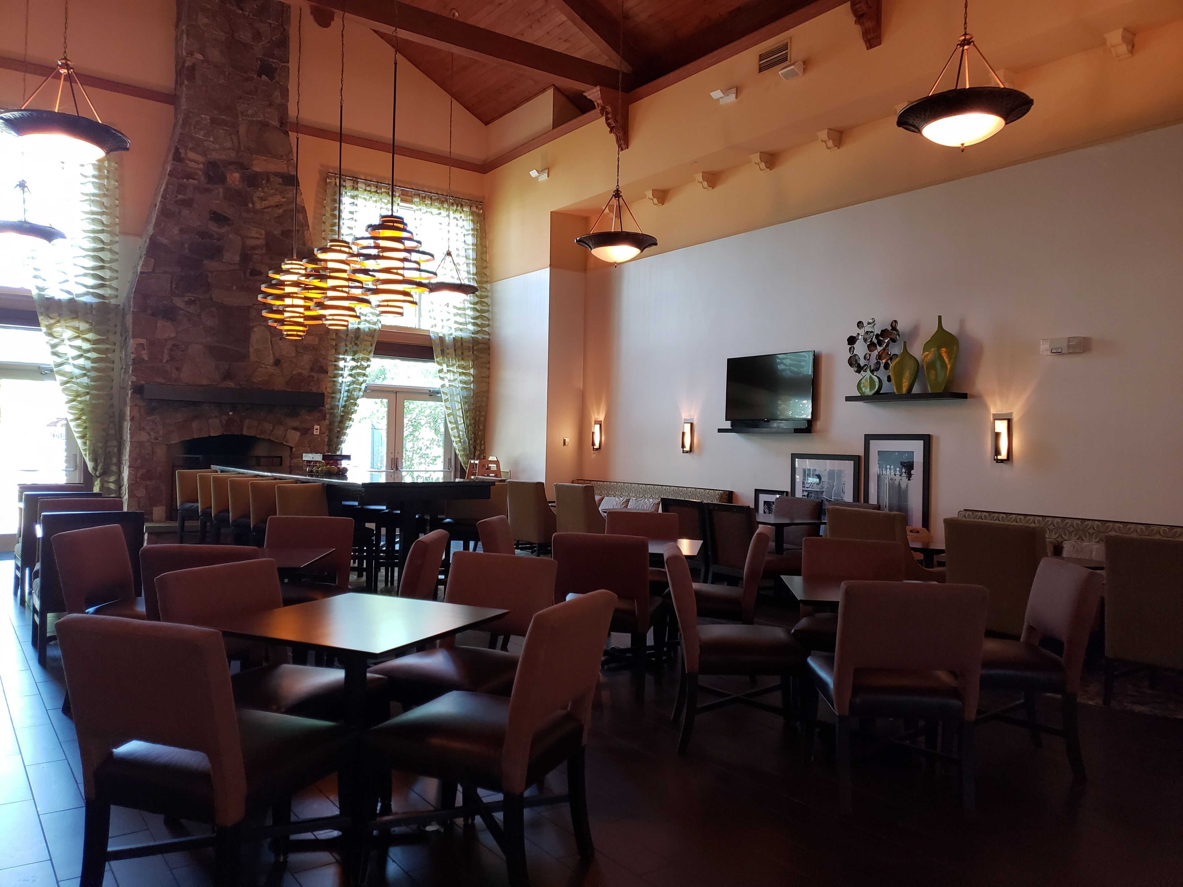 Ein Restaurant mit hohen Decken, Steinwänden und hängenden Pendelleuchten. Tische und Stühle sind zum Essen angerichtet.