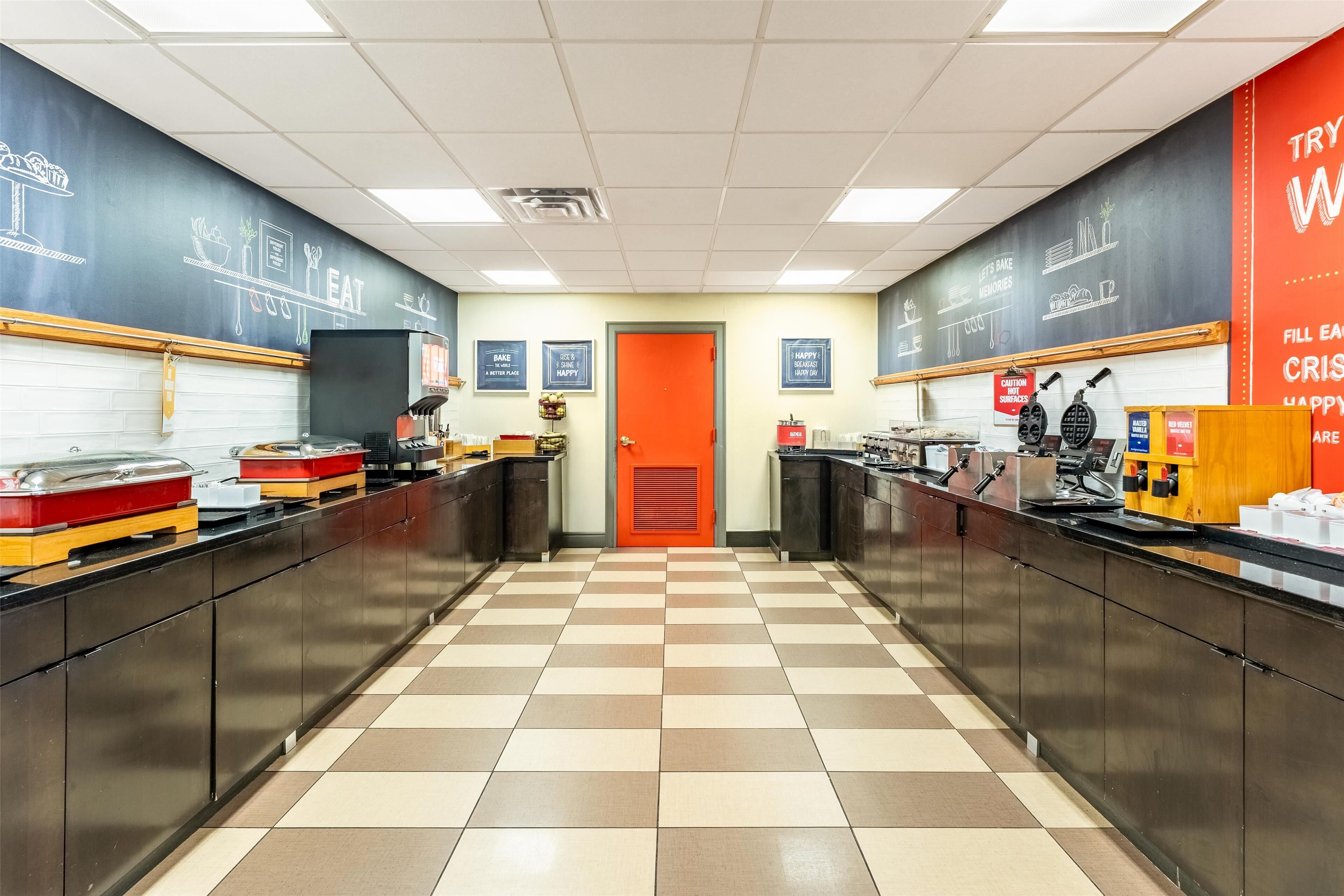 A kitchen with checkered flooring, a red door, and various appliances and utensils on the counters.