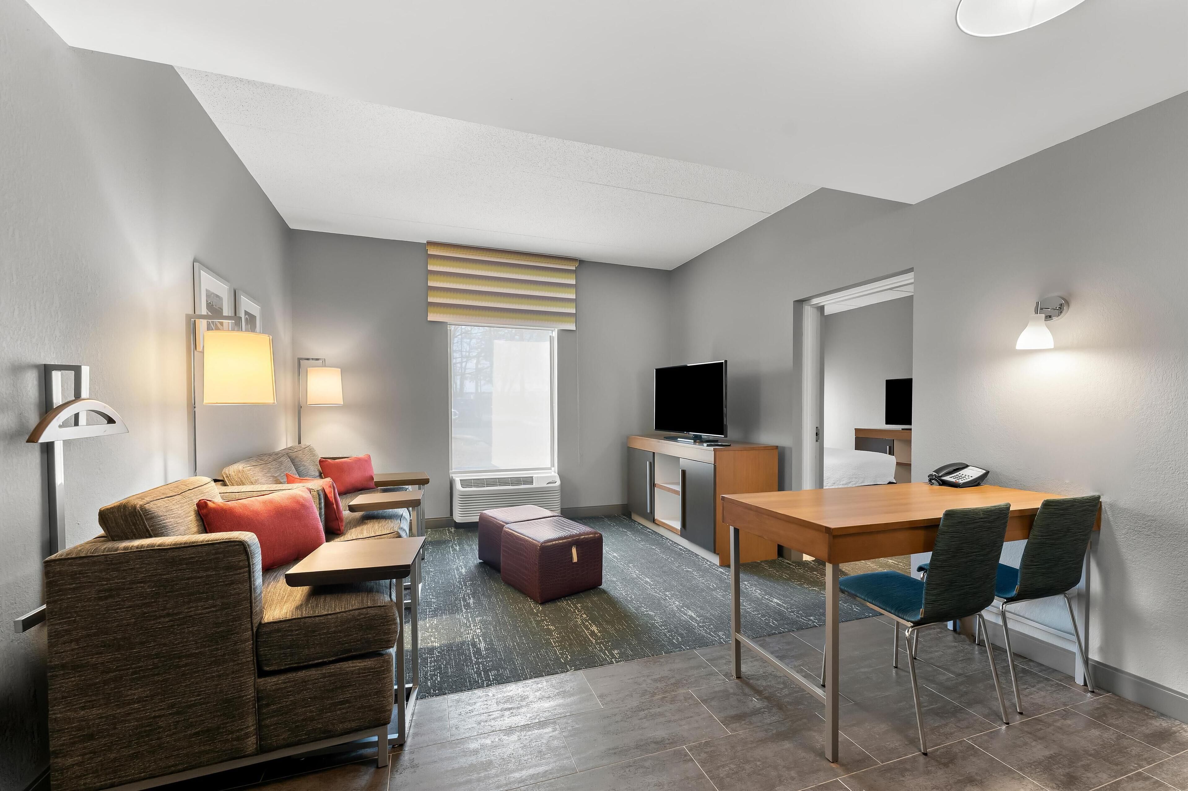 Una habitación de hotel moderna con sofá, una mesita, televisor y escritorio con sillas.