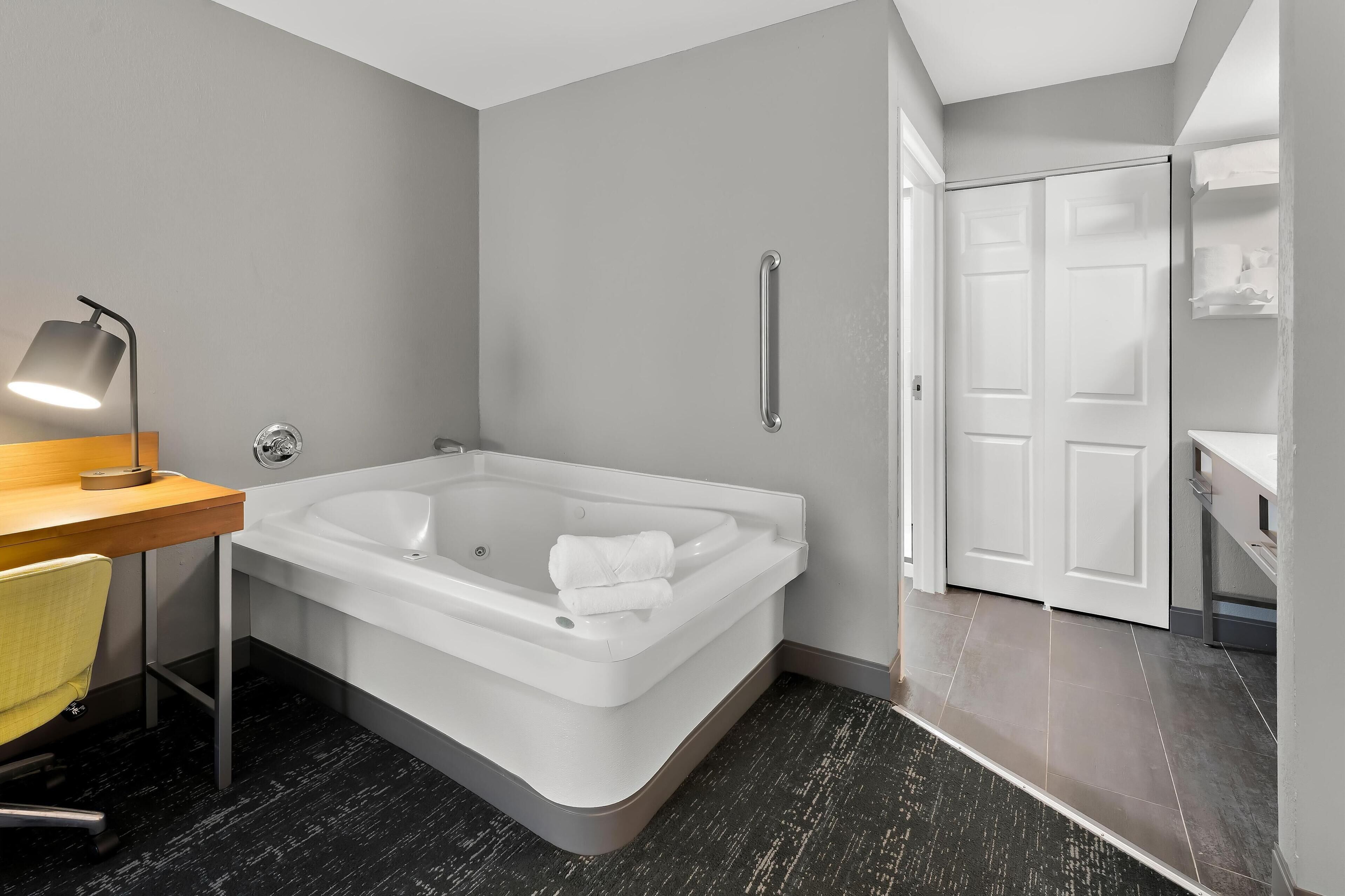 Un baño moderno con una bañera grande, un escritorio con lámpara y zona de ducha.