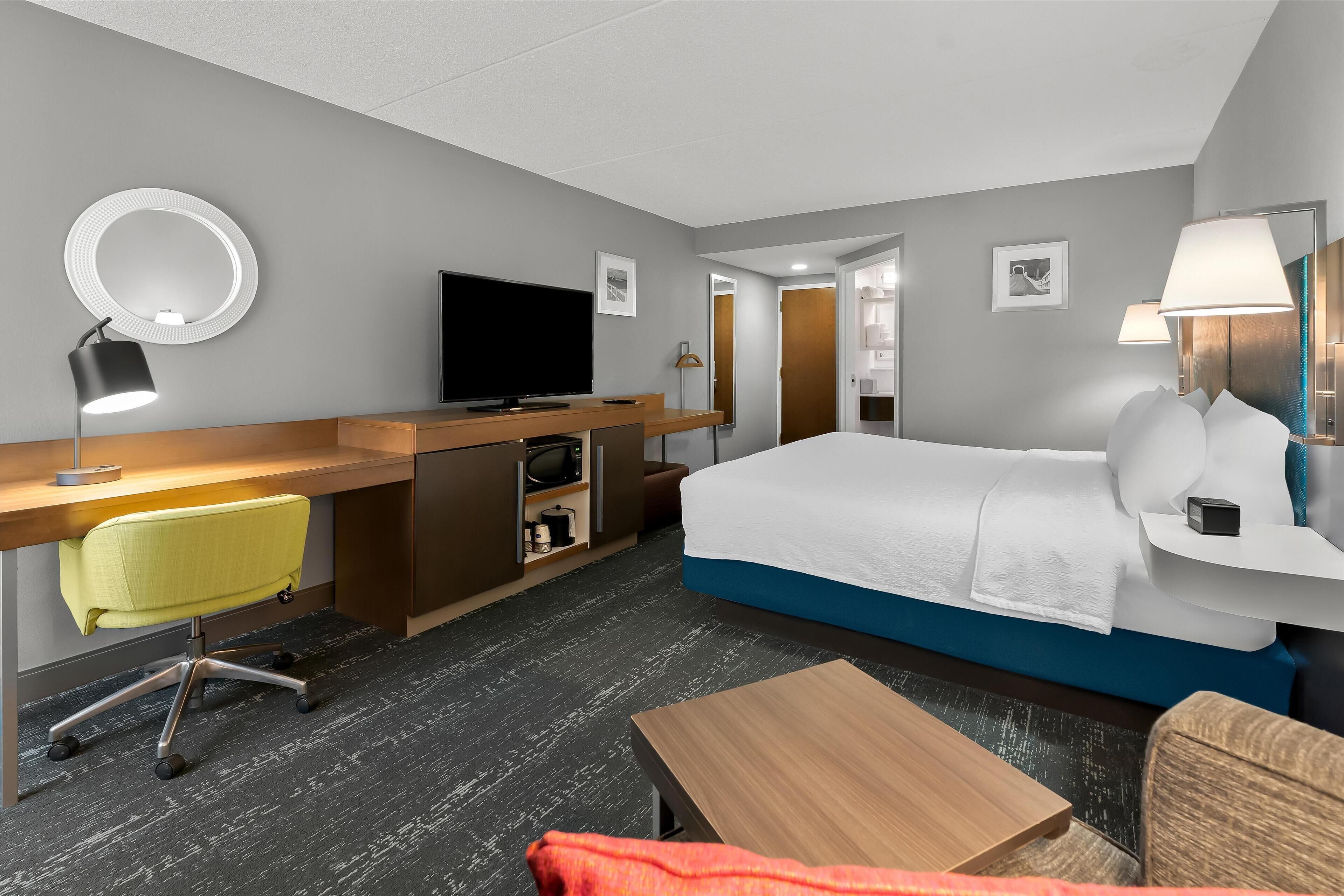 A modern hotel room with a bed, desk, chair, and a television.