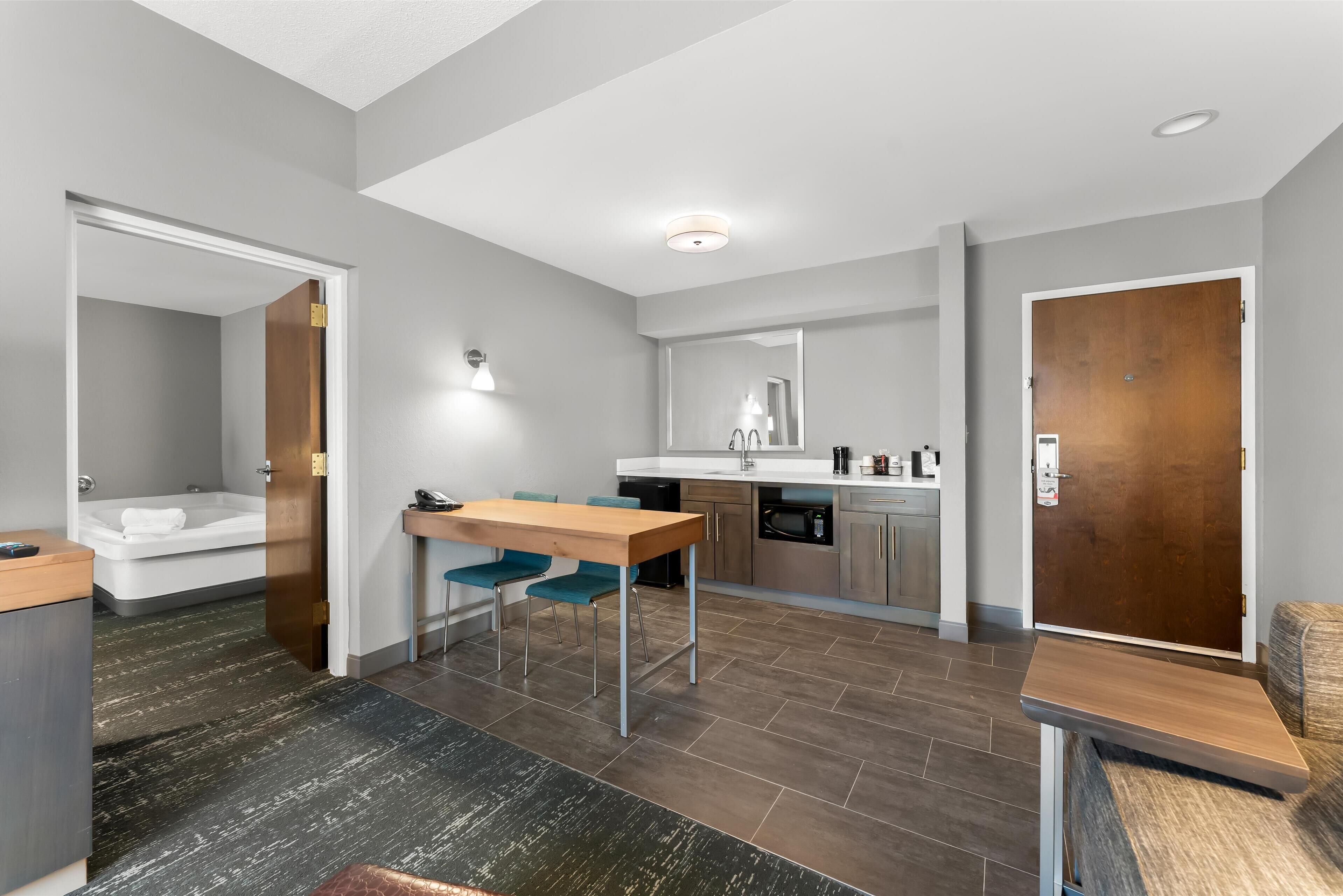 A modern hotel room with a kitchenette, a dining area, and a bathroom.