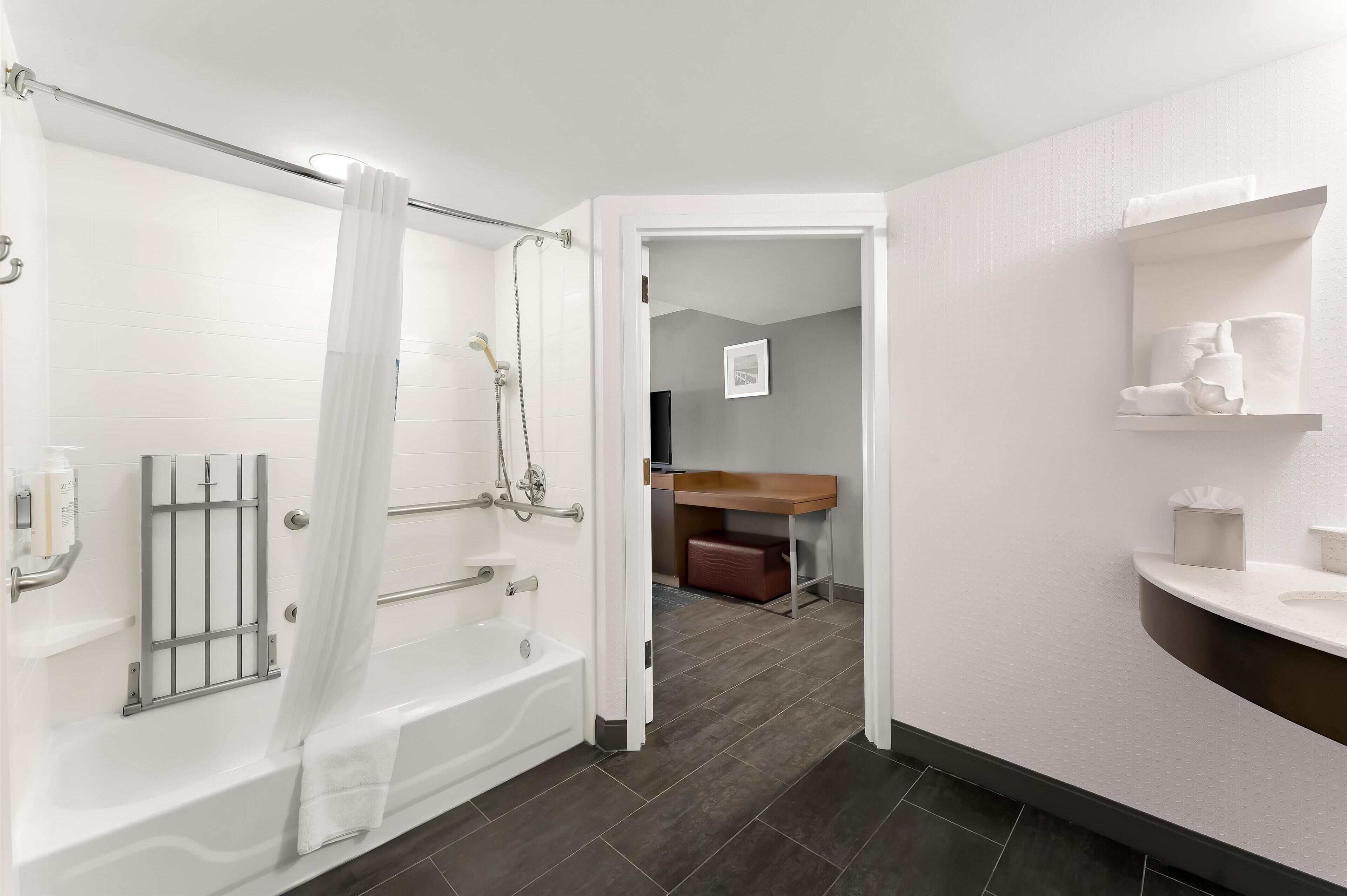 A modern bathroom with a bathtub, shower, and toilet. There is a towel rack and a shelf with toiletries.