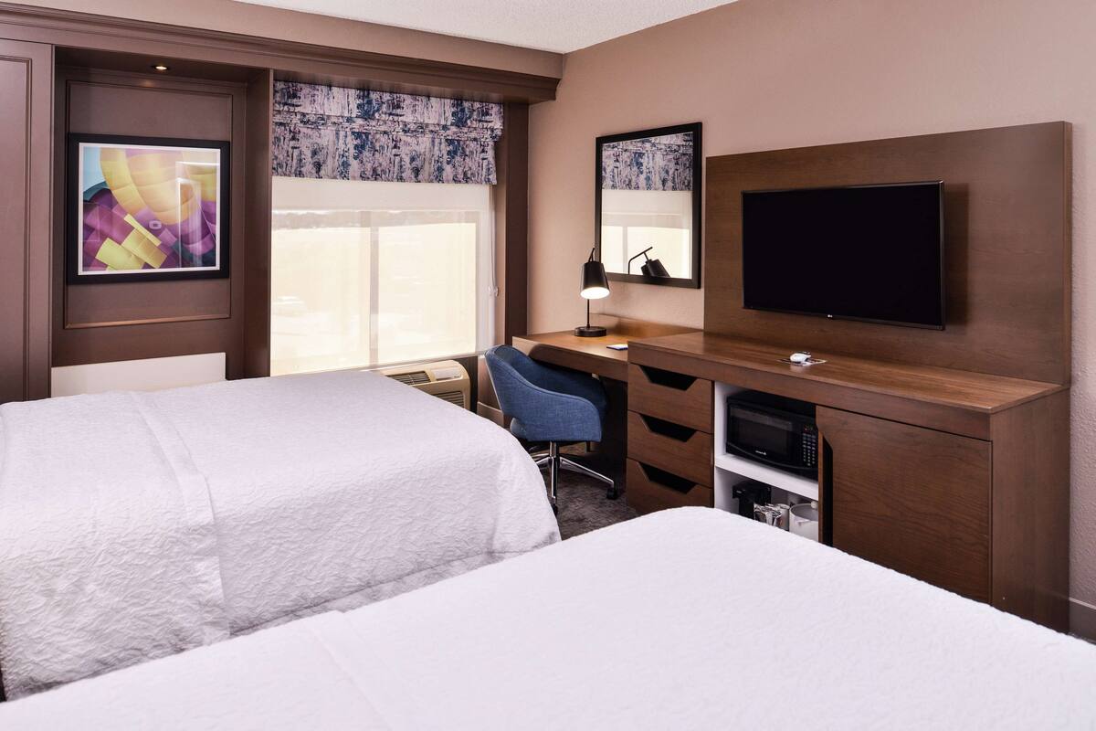 A hotel room with two beds, a desk with a chair, a TV, and a microwave.