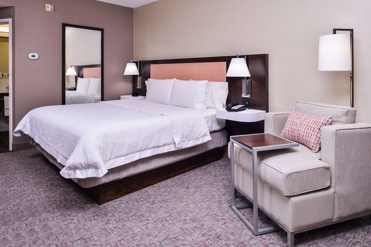 A hotel room with a large bed, bedside tables, a chair, and a desk.