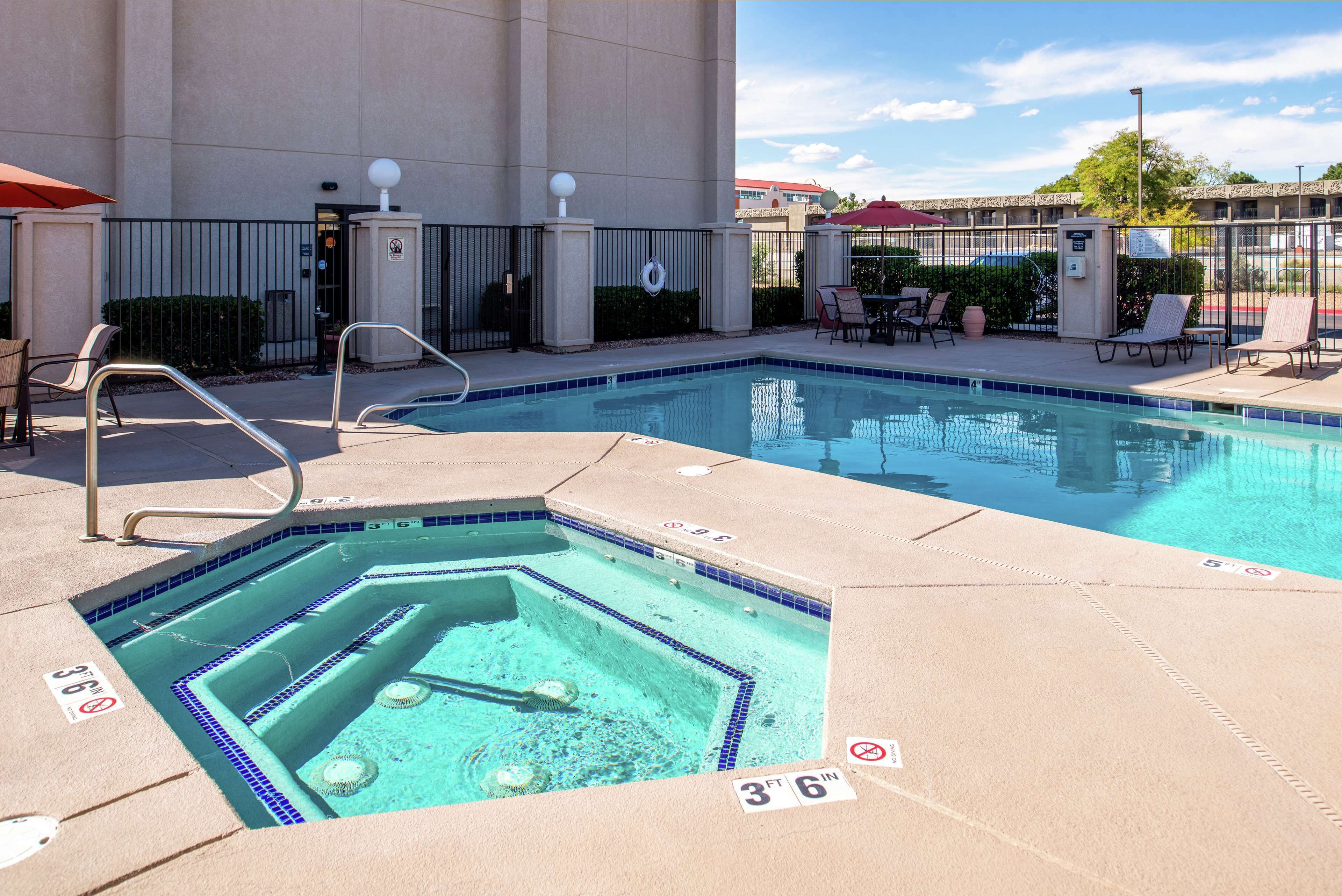 Un área de piscina con jacuzzi, sillas de descanso y un patio cercado.