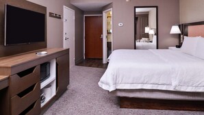 Une chambre d’hôtel avec un grand lit, un téléviseur à écran plat, un bureau en bois et une armoire.
