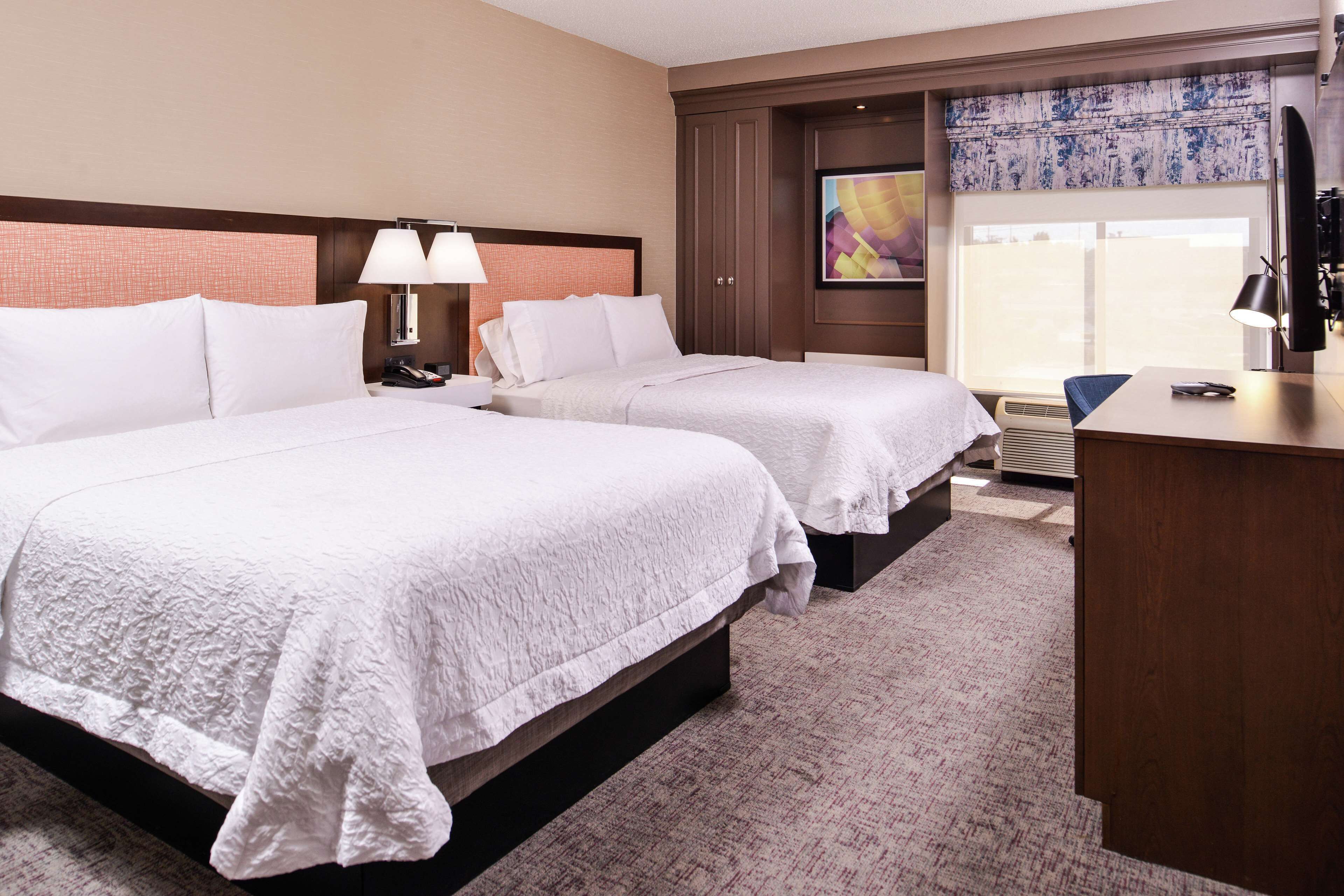 A hotel room with two beds, a desk, and a large window with a view.