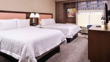 A hotel room with two beds, a desk, and a large window with a view.