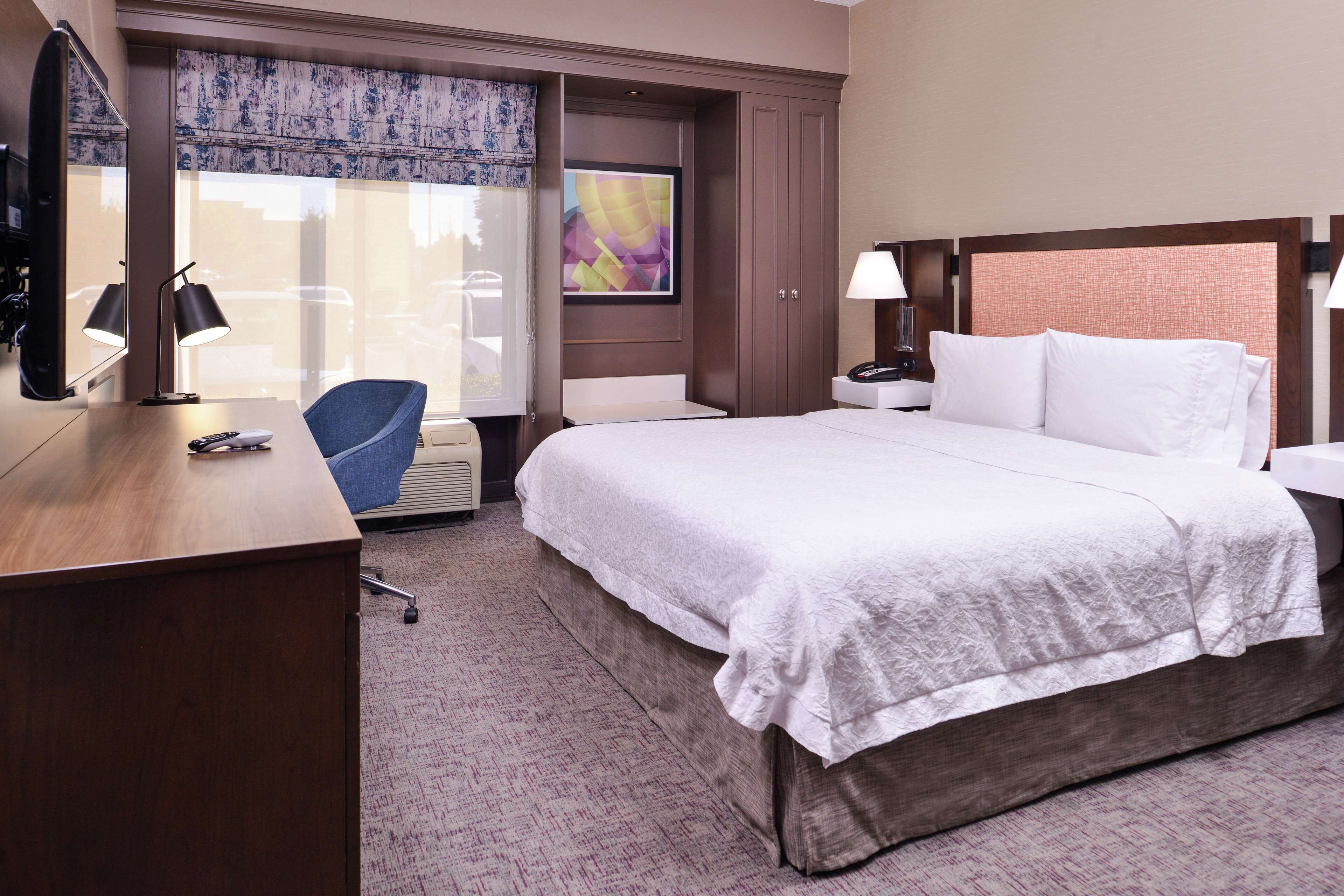 A hotel room with a large bed, a desk with a chair, a TV, and a window with a view of the outside.