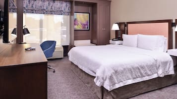 A hotel room with a large bed, a desk with a chair, a TV, and a window with a view of the outside.