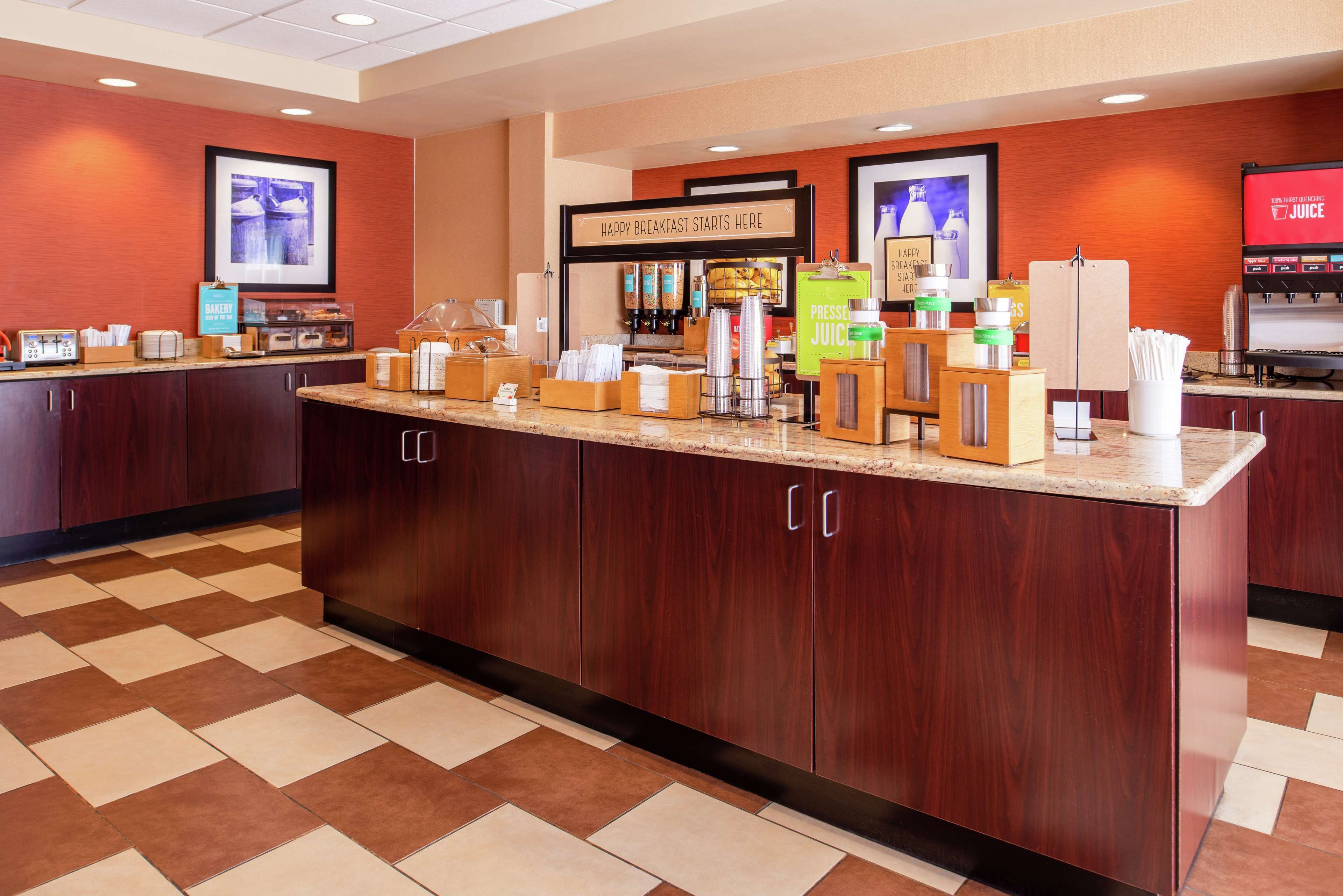 A breakfast bar with a coffee station, a sign reading "Happy Breakfast Starts Here," and a juice dispenser.