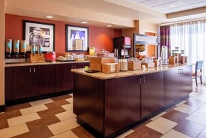 A hotel breakfast area with a large counter, coffee dispensers, and a television.