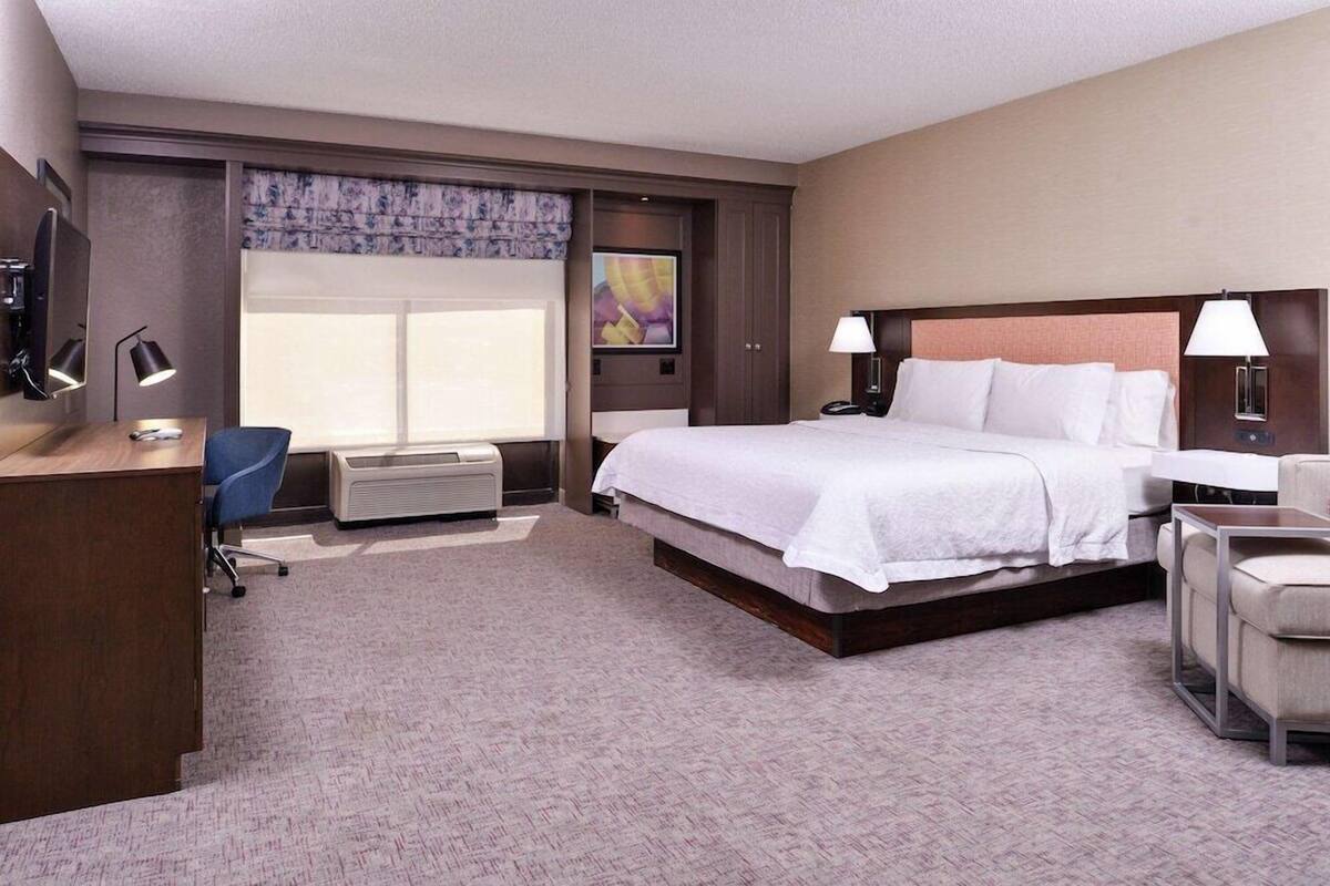 A hotel room with a large bed, a desk with a chair, a TV, and a window with curtains.