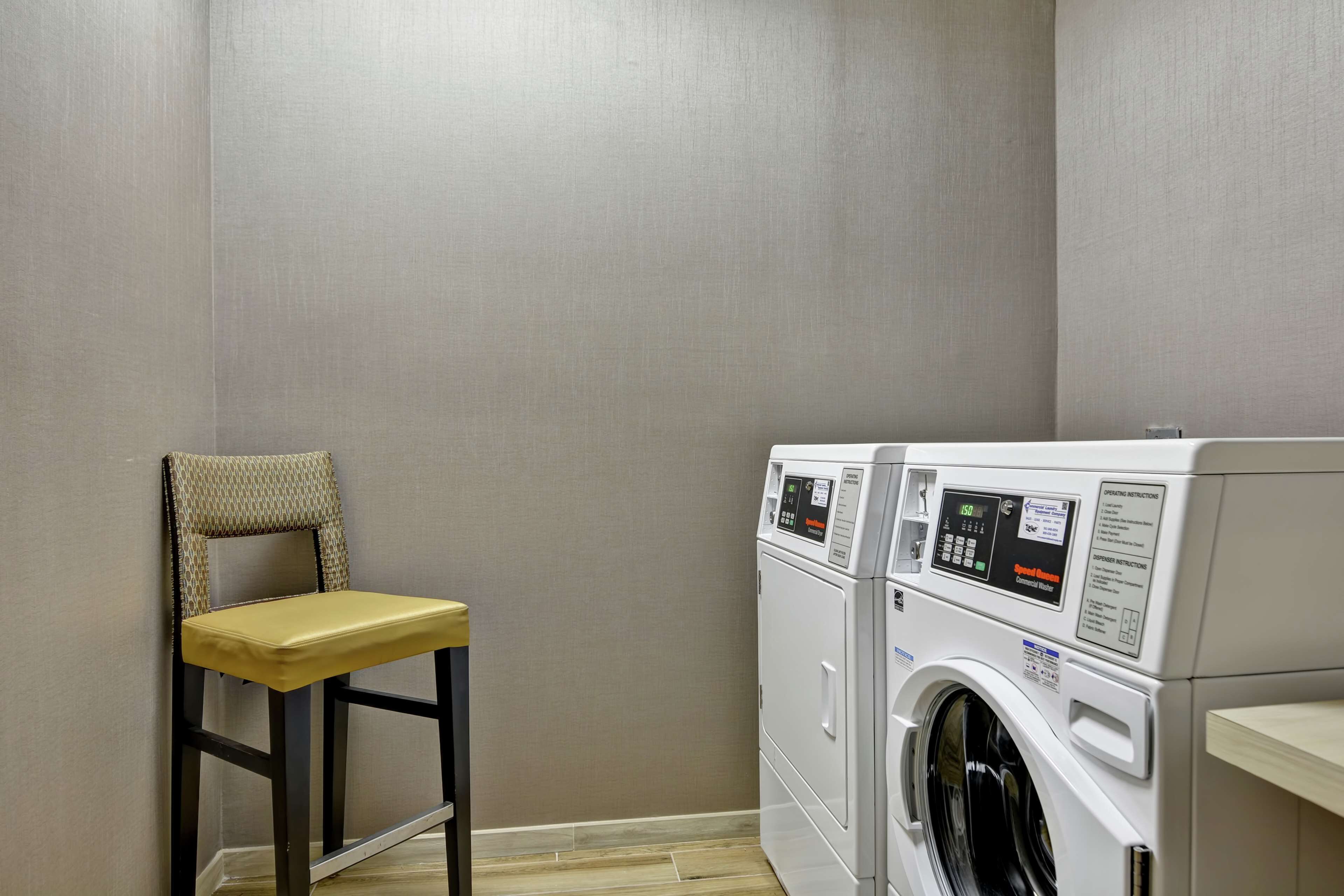 A laundry room with a washing machine and dryer, a chair, and a wooden floor.