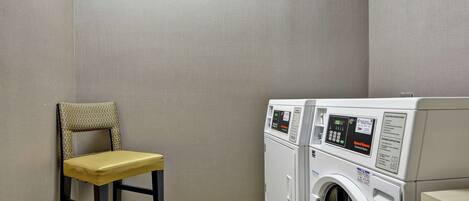A laundry room with a washing machine and dryer, a chair, and a wooden floor.