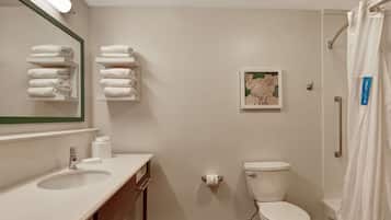 Une salle de bain avec un lavabo, des toilettes et un rideau de douche. Il y a des serviettes sur une étagère et un tableau encadré au mur.